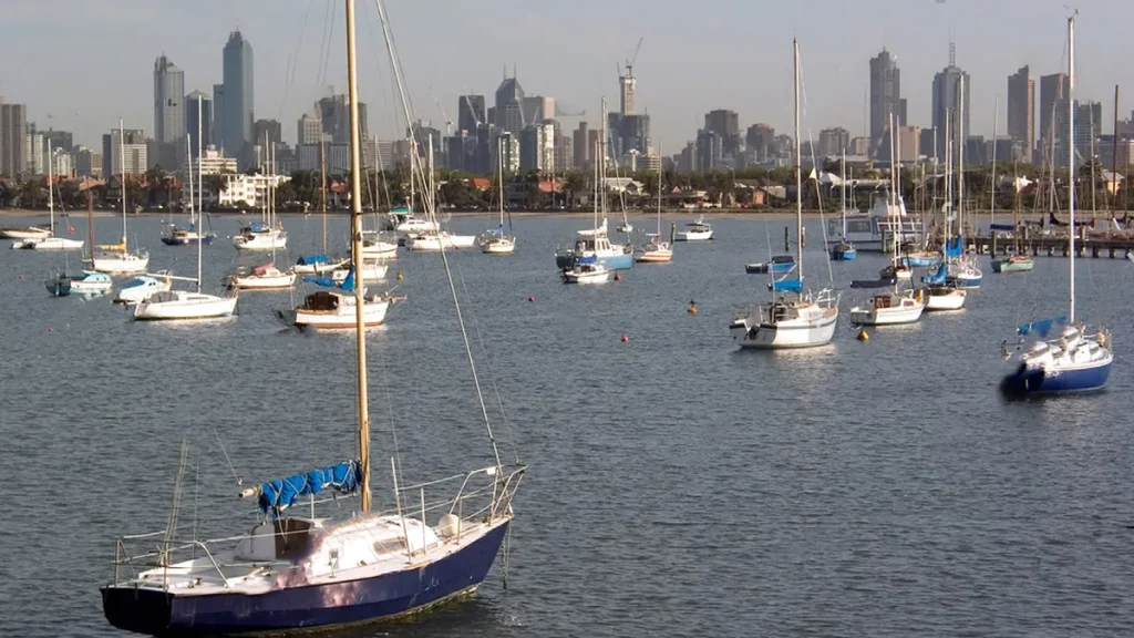 Sailboats moored in calm waters with the Melbourne skyline in the distance